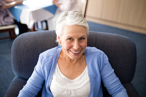 High angle view of smiling senior woman sitting on armchair at retirement home