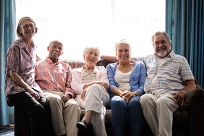 Portrait of smiling senior people sitting on couch against window at nursing home