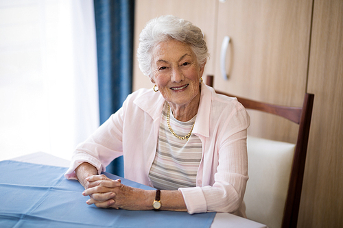 Portrait of smiling senior woman sitting with hands clasped at table in nursing home