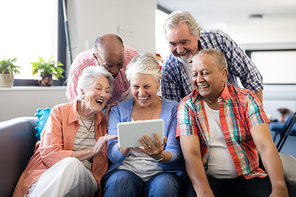 Cheerful senior friends looking at digital tablet while resting in nursing home