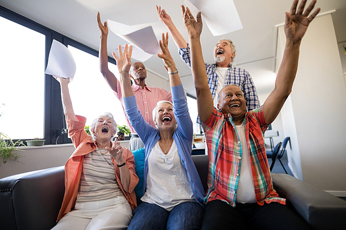 Excited senior people with arms raised throwing papers in nursing home