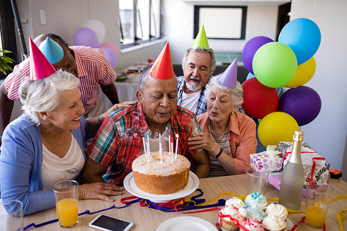 Senior man blowing candles on birthday cake while enjoying with friends at party