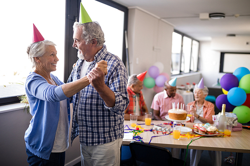 Smiling senior couple dancing by friends enjoying at birthday party