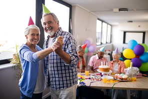 Portrait of smiling senior couple holding hands while standing against friends during birthday party