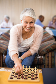 Portrait of confident senior woman playing chess at table while sitting on couch in nursing home