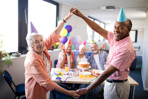 Portrait of smiling senior couple making frame against friends by holding hands while enjoying in birthday party