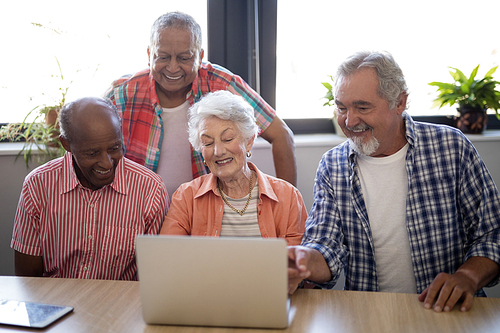 Happy senior people using laptop at table against window in nursing home