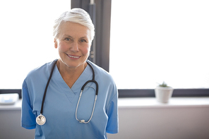 Portrait of senior female doctor standing against window in nursing home