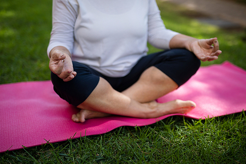 Mid section of senior woman meditating while sitting on exercise mat at park