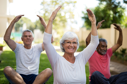 Smiling senior people exercising with arms raised while sitting on field at park