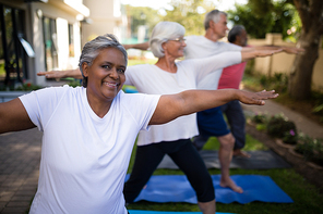 Portrait of smiling senior woman doing stretching exercise with friends at park