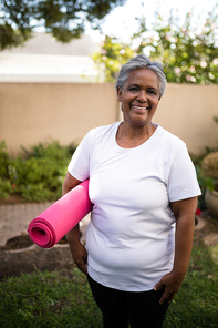 Smiling senior woman carrying exercise mat while standing at park