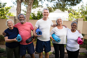 Portrait of laughing senior friends carrying exercise mats while standing at park