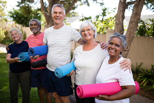 Portrait of happy multi-ethnic friends carrying exercise mats while standing at park