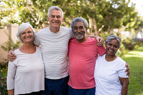 Portrait of smiling senior friends standing with arms around at park