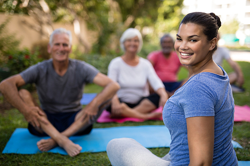 Smiling trainer sitting with senior people while exercising at park