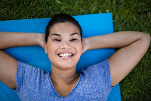 High angle portrait of smiling trainer lying on exercise mat at park