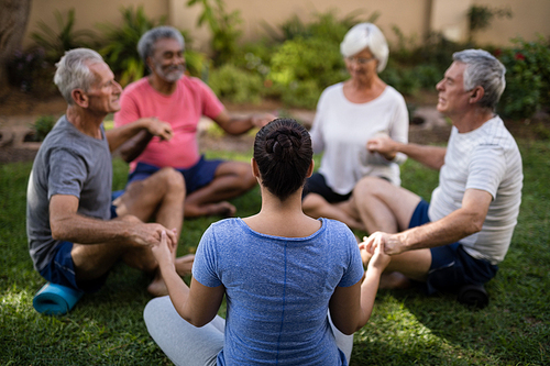 Trainer holding hands and meditating with senior men and women while exercising at park