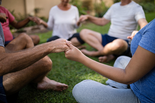 Cropped image of trainer holding hands with senior people while sitting at park
