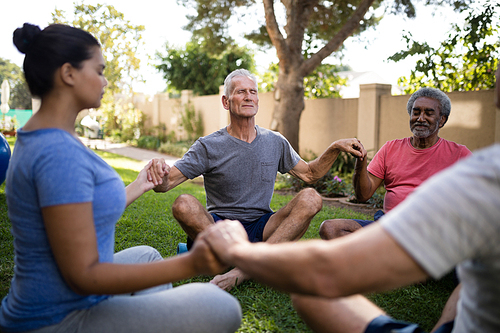 Trainer meditating with senior men and women while holding hands at park