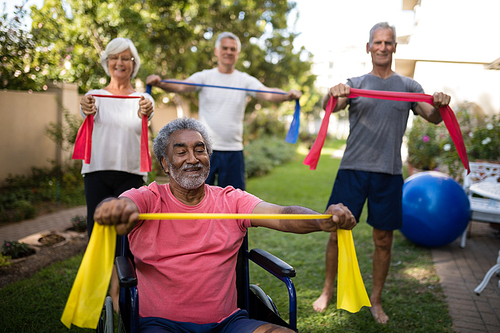 Physically impaired senior man holding ribbon with friends while exercising at park