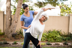 Smiling trainer assisting senior woman with hand raised while exercising at park
