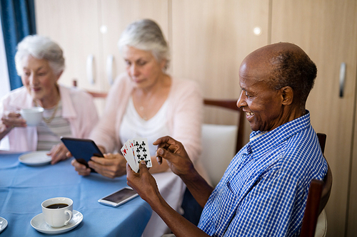 Senior man playing cards with friends while having coffee at table in nursing home