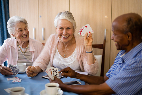 Happy senior people playing cards while having coffee at nursing home
