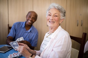 Portrait of senior woman playing cards with friend while sitting at table in nursing home