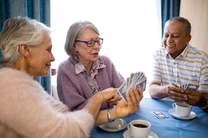 Smiling senior woman showing cards to friends while playing at table in nursing home