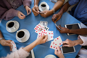 Overhead view of senior people playing cards while having coffee at table in nursing home
