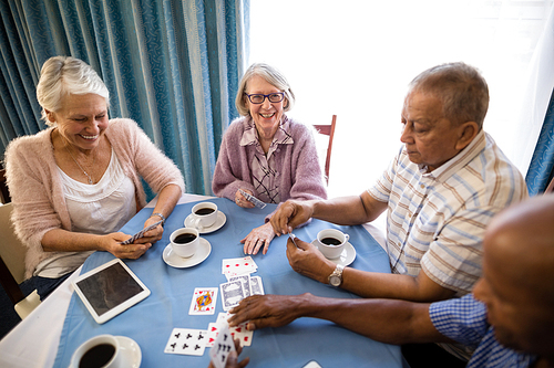 High angle view of senior friends playing cards while having coffee at table in nursing home