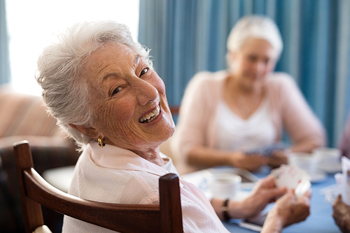Smiling senior woman playing cards with friends at table in nursing home