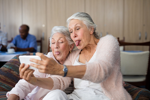 Senior women making face while taking selfie through smart phone at nursing home