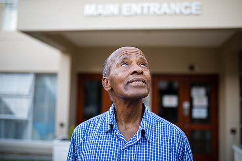 Thoughtful senior man looking up while standing against house