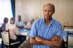 Portrait of senior man standing with arms crossed against friends at nursing home