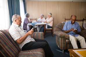 Senior men using mobile phone while females having coffee in nursing hoome