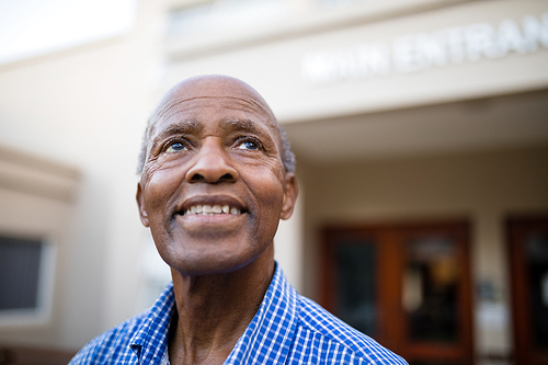 Close-up of thoughtful senior man smiling while looking up at nursing home