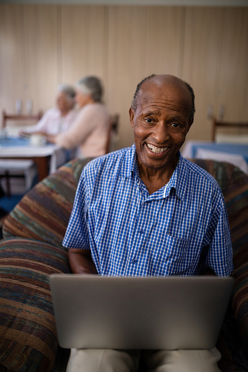 Portrait of happy senior man using laptop while sitting on sofa at nursing home