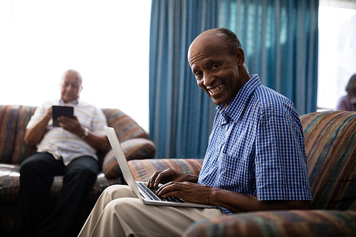 Portrait of senior man using laptop by friend at nursing home