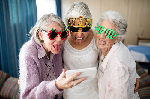 Senior women wearing novelty glasses making face while taking selfie through mobile phone at nursing home