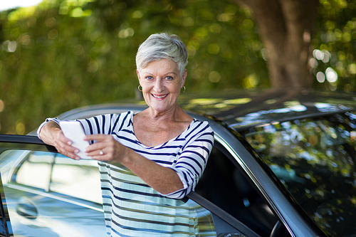 Portrait of senior woman holding phone while leaning on car door