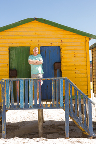 Portrait of smiling senior man standing at beach hut on sunny day