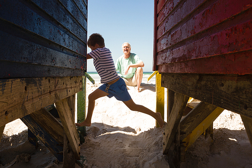 Happy boy playing with grandfather by huts at beach