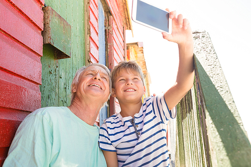 Happy boy with grandfather taking selfie  while sitting by wall