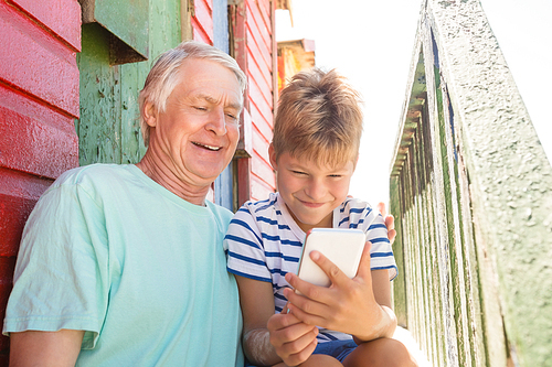 Happy boy with grandfather using smart phone while sitting by wall at beach