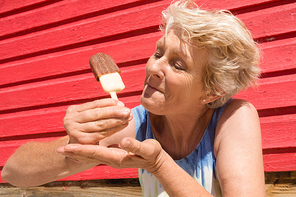 Senior woman eating ice cream while standing by hut at beach