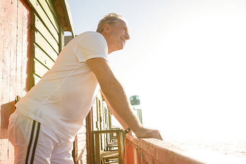 Senior man looking away while leaning on railing at beach