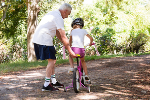 Grandfather teaching his granddaughter how to ride a bicycle in the forest