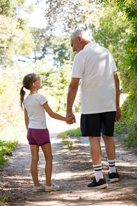 Grandfather and granddaughter holding hands while walking in the forest
